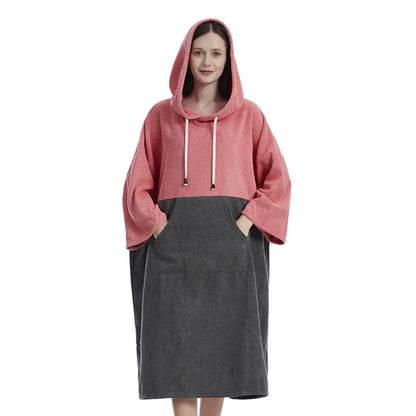 Woman wearing a pink and gray hooded towel poncho, perfect for quick drying after surfing or swimming at the beach.