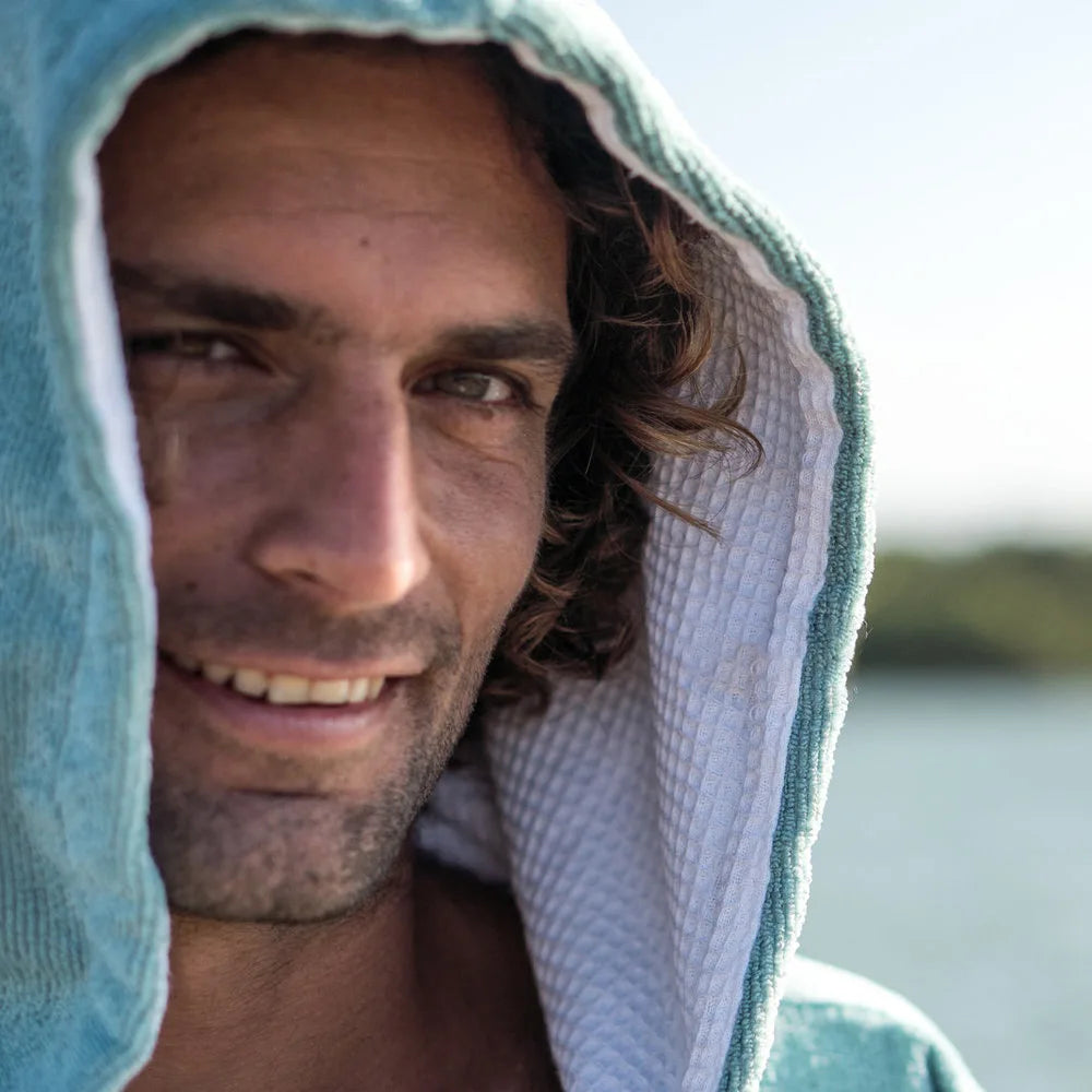 Man wearing a teal swimming diving hooded bathrobe, smiling by the water, showcasing comfort and style for water activities.